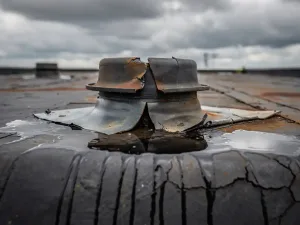 Verouderde rubberen dakdoorvoer met scheuren, loslatende flashing en regenwater op slijtagegevoelige bitumineuze dakbedekking.