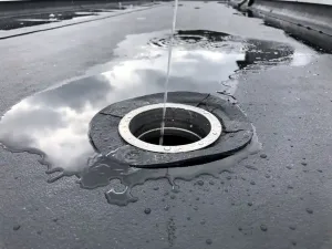 Dakafvoer omgeven door EPDM-membraan op plat dak, met regenwater dat afstroomt onder bewolkte Nederlandse lucht.