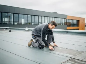 Dakspecialist inspecteert bitumineuze membraanlaag op plat commercieel dak bij bewolkt daglicht.