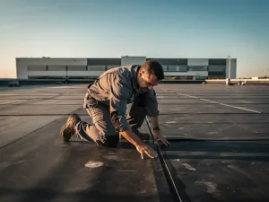 Dakspecialist inspecteert naad van plat commercieel dak met EPDM-membraan bij warm ochtendlicht.