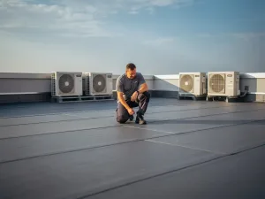 Dakspecialist inspecteert naadloos bitumineus plat dak van modern appartementencomplex met zichtbare HVAC-units en borstweringen.